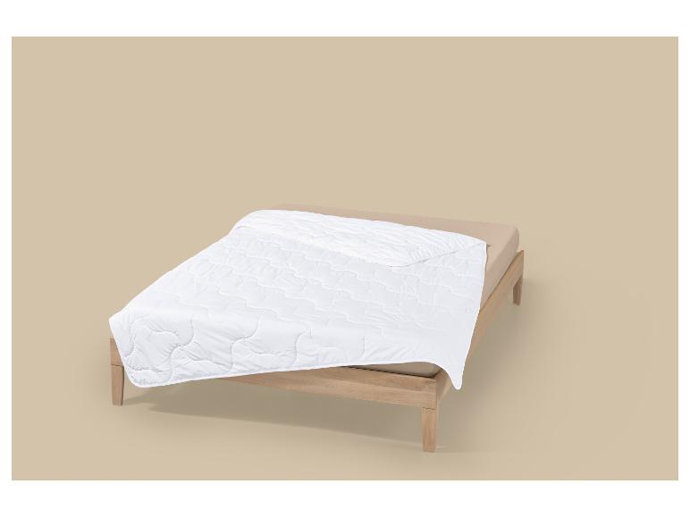 Bed met wit gewatteerd dekbed en beige lakens op een neutrale achtergrond.