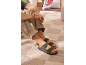 Groene herensandalen met gespen, beige broek en groen T-shirt, zittend op een tapijt.