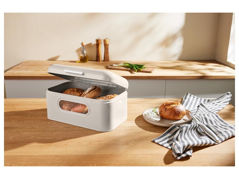 Een beige broodtrommel met brood op een houten tafel in een keuken.