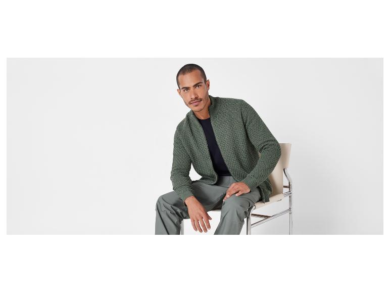 Man in een groen vest en broek zit op een stoel.