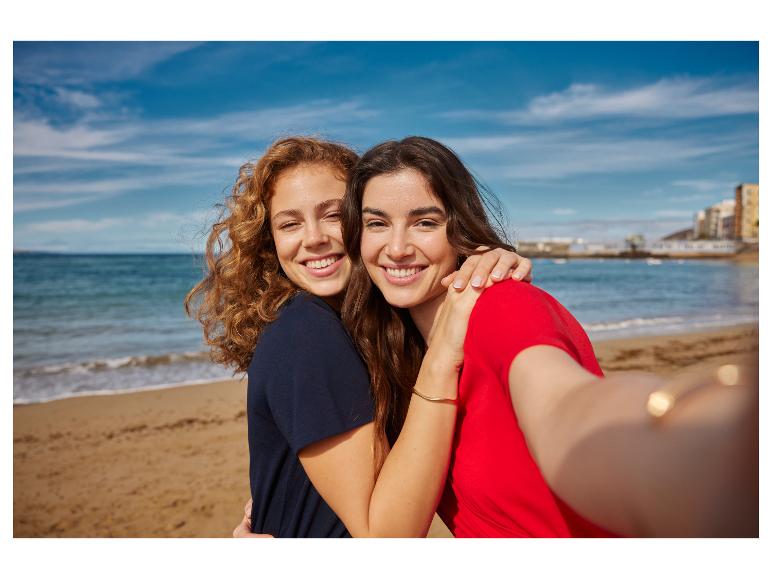 Twee lachende jonge vrouwen maken een selfie op het strand met de zee op de achtergrond.