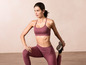 Vrouw in roze sportbeha en leggings strekt haar been.