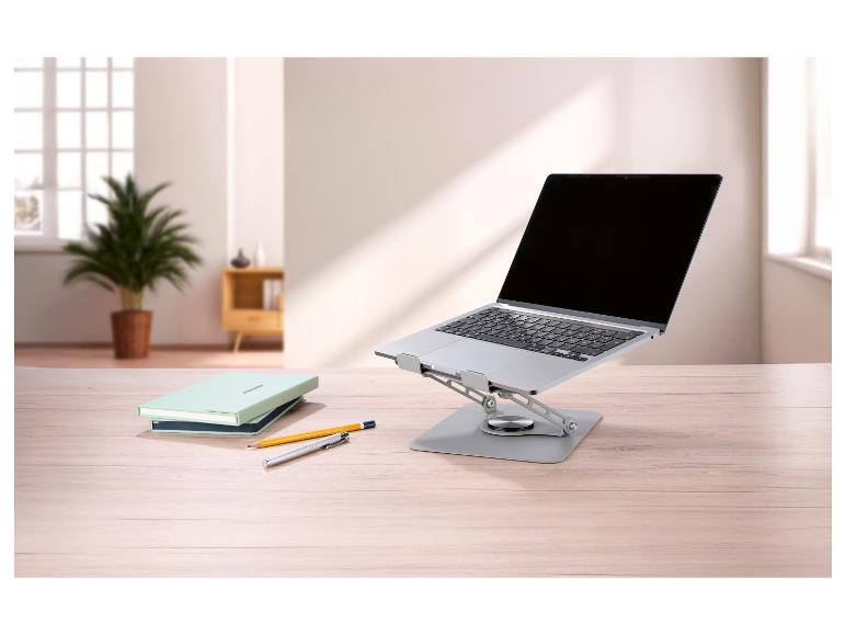 Laptop op een verstelbare standaard met notitieboekjes en pennen op een bureau.