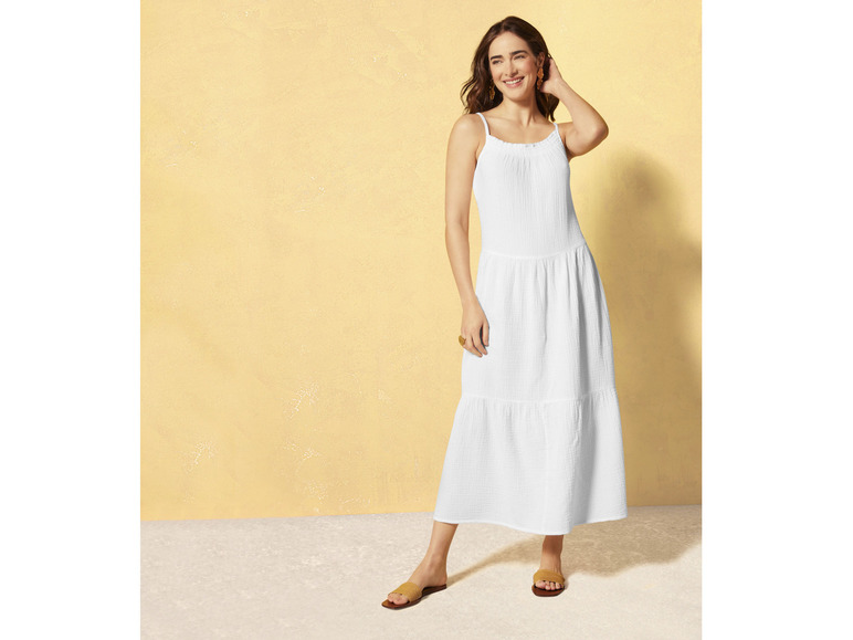 Een vrouw draagt een witte jurk met spaghettibandjes en sandalen.