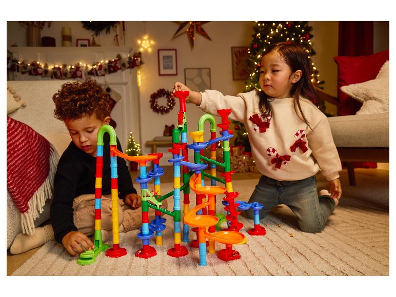 Twee kinderen spelen met een kleurrijke knikkerbaan op een tapijt in een kerstversierde kamer.
