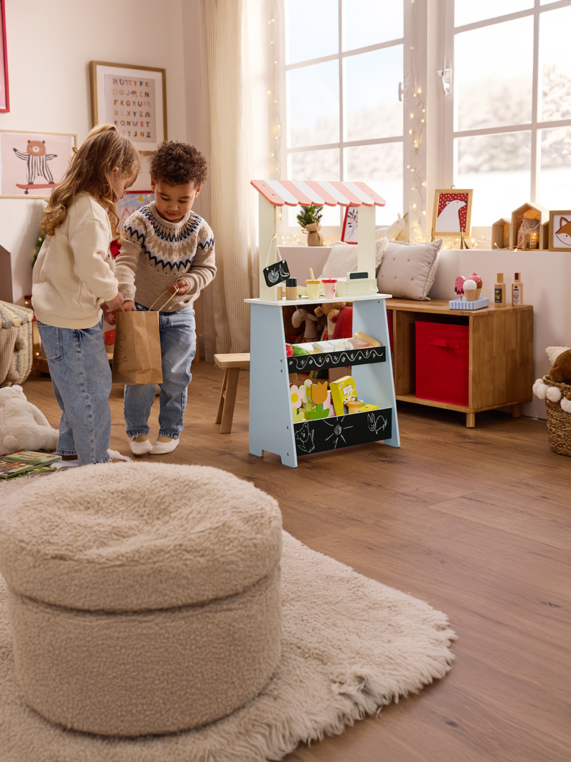 Twee kinderen spelen met een houten marktkraam, met een meisje dat een papieren zak vasthoudt.