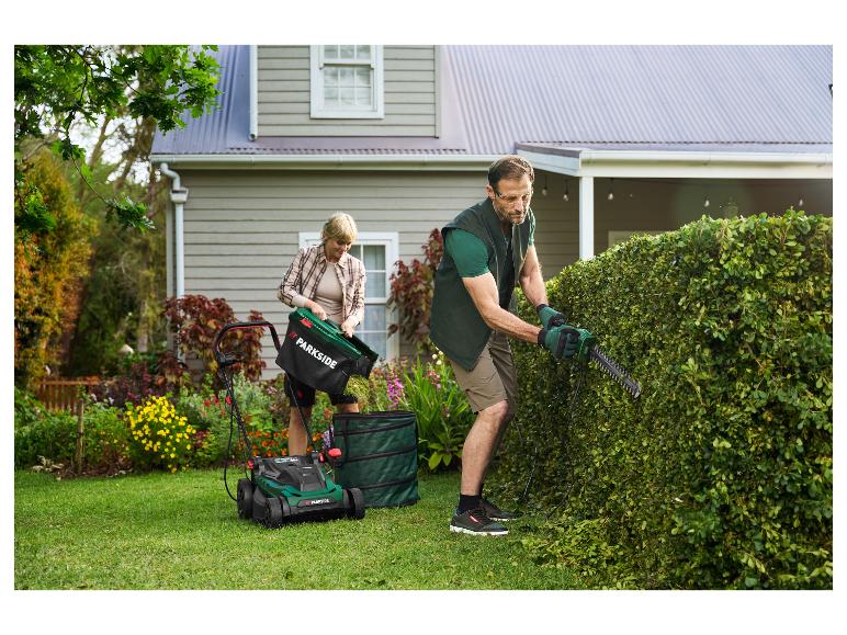 Man snoeit heg, vrouw leegt grasmaaier in de tuin.