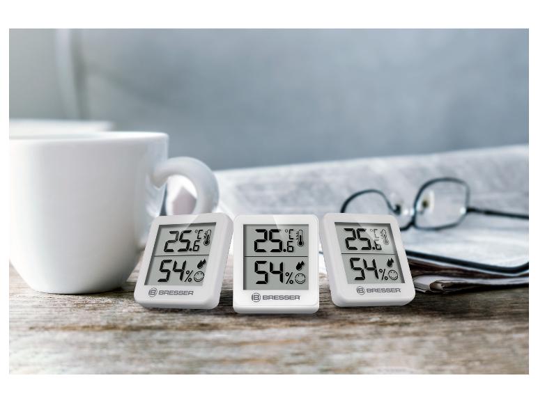 Drie witte BRESSER digitale thermo-hygrometers op een houten tafel.
