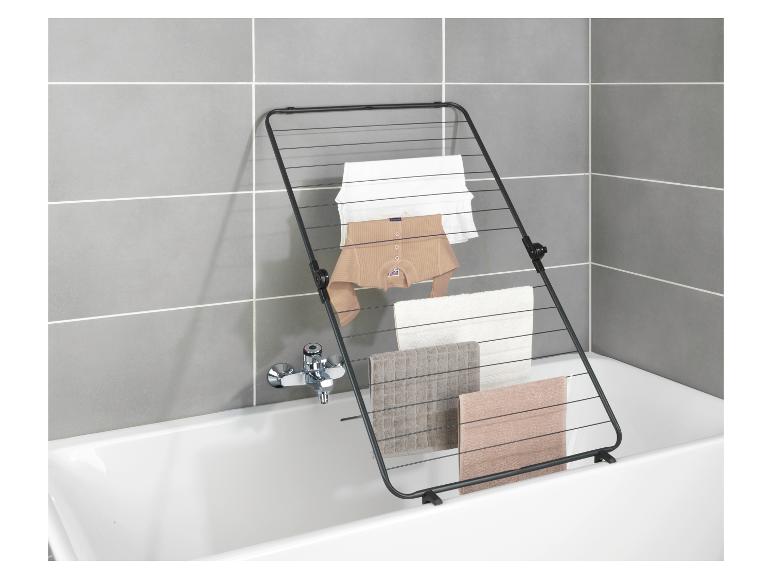 Een zwart metalen droogrek boven het bad houdt kleding en handdoeken in een moderne badkamer.