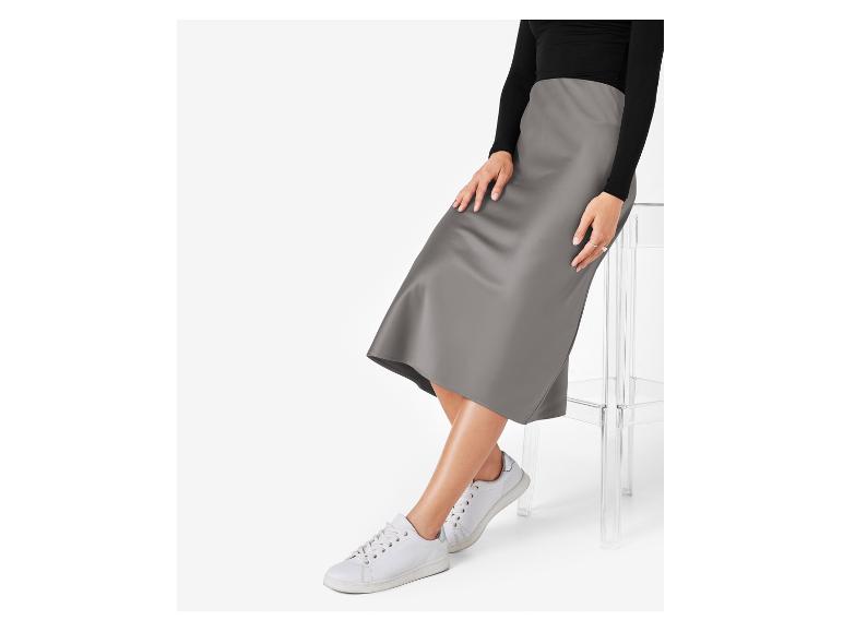 Een vrouw draagt een grijze satijnen rok en witte sneakers.