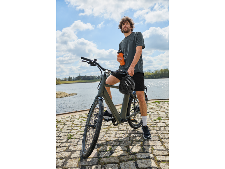 Man op een fiets bij het water met een drinkfles in zijn hand.