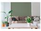 Woonkamer met groene muur, grijze bank, kussens, plaids, planten en witte salontafel.