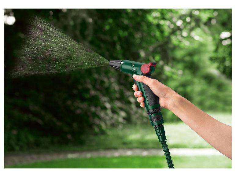 Hand houdt groen tuinspuitpistool vast met waterstraal tegen wazige groene achtergrond.