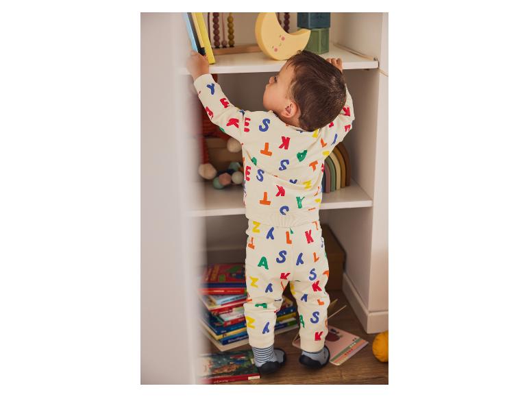 Een klein kind in een pyjama met letters pakt boeken van een plank.