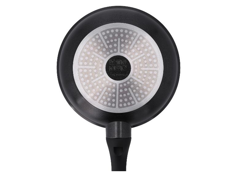 Onderkant van een zwarte koekenpan met een ronde, gedessineerde metalen bodem en een zwart handvat.