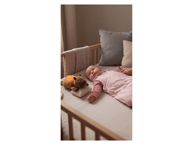 Baby slaapt in wieg in roze slaapzak met oplichtend knuffeldier.