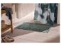 Groene badmat met patroonrand op beige tegels, naast een houten rek.