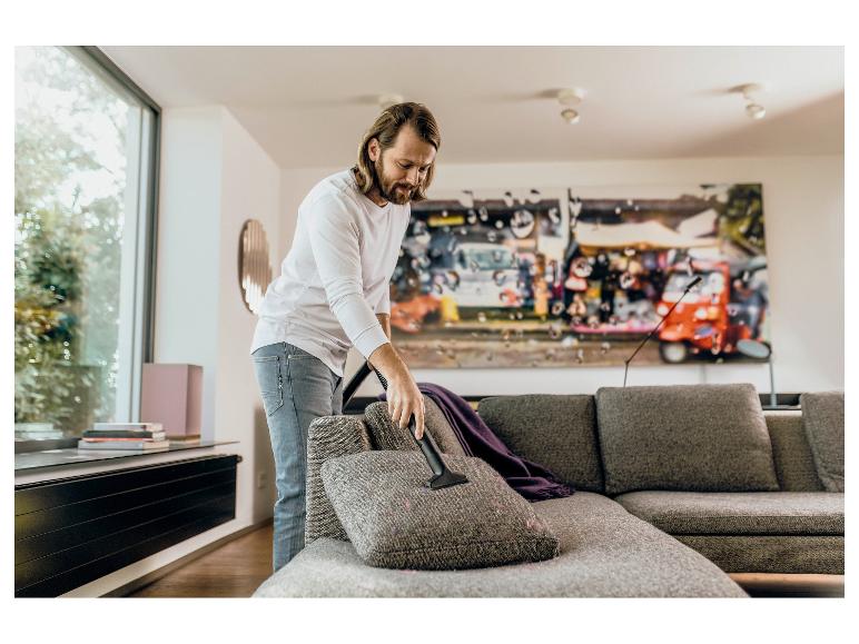 Man stofzuigt de bank met een kruimeldief in de woonkamer.