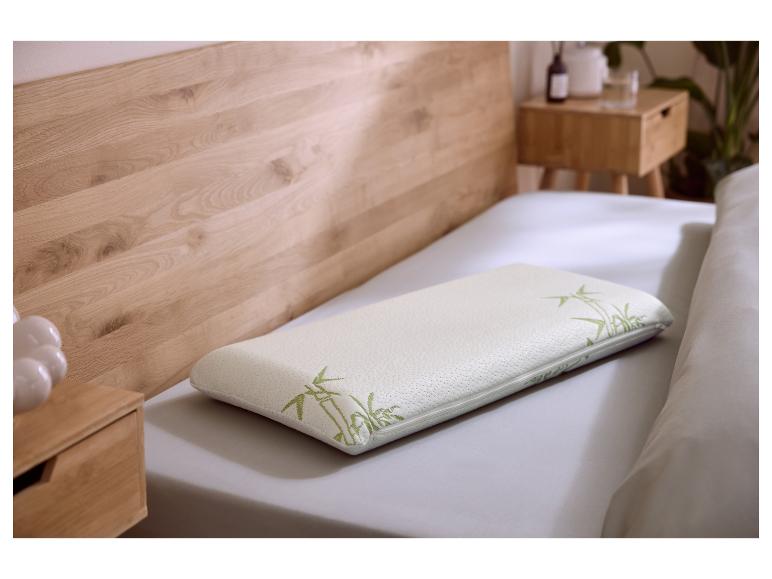 Wit traagschuim kussen met groene bamboeprint op een bed met houten hoofdbord.