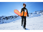 Jongere in ski-jas en broek met snowboard op besneeuwde berghelling.