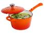Oranje steelpan met deksel, gevuld met groene soep, gegarneerd met dille en roze peperkorrels.