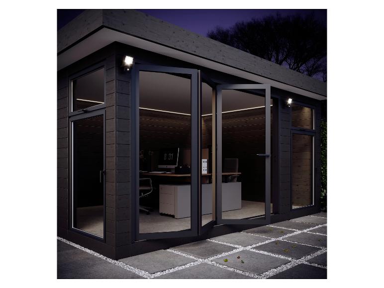 Modern tuinkantoor met grote glazen deuren, binnenverlichting en buitenverlichting 's nachts.