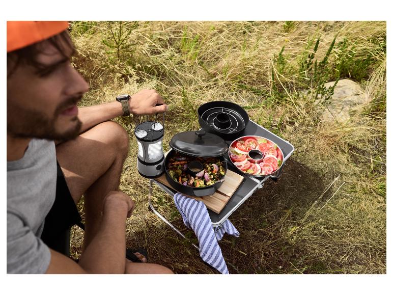 Man kookt buiten met een draagbare grill, lantaarn en verse salade.