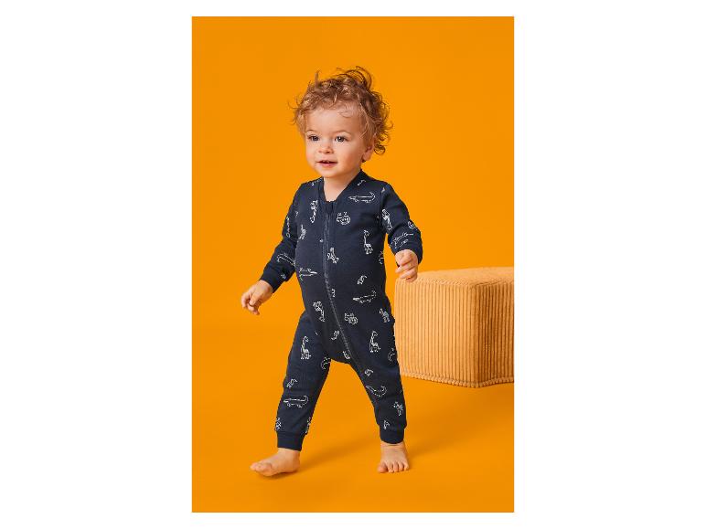 Peuter in een marineblauwe romper met dierenprint, lopend op een oranje achtergrond.