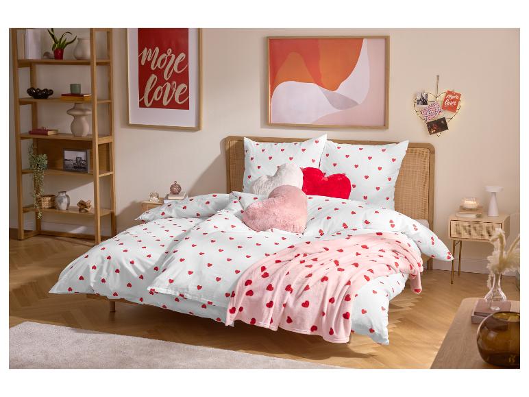 Slaapkamer met tweepersoonsbed, wit beddengoed met rode hartjes en hartvormige kussens.