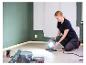 Vrouw stelt LIVARNO® werklamp „The Painter+“ af in een kamer met geverfde muren.