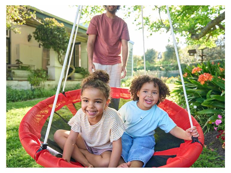 Twee kinderen in een rode schommel in de tuin.