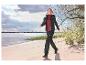 Vrouw in een zwart gewatteerd jack en zwarte outdoorbroek loopt op een zandstrand.