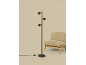 Zwarte vloerlamp met drie verstelbare spots naast een beige fauteuil.