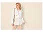 Vrouw in witte getextureerde blazer, lichtroze T-shirt en beige broek, met schoudertas.