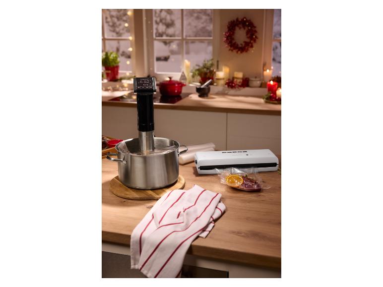 Sous vide-koker in een pan, vacuümsealer en vacuümverpakt voedsel op een aanrecht.