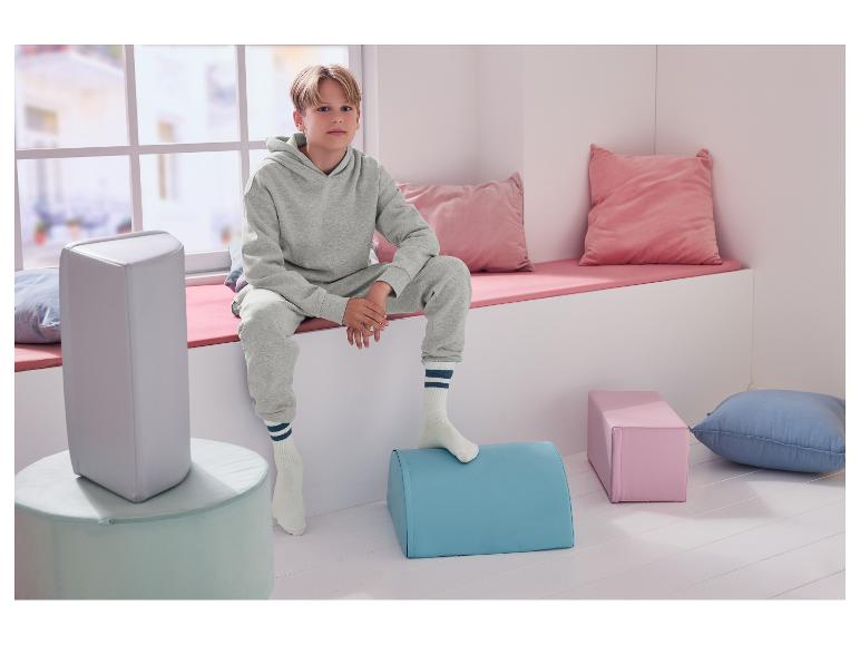 Een jongen zit op een vensterbank, omringd door kussens en kleurrijke poefs.