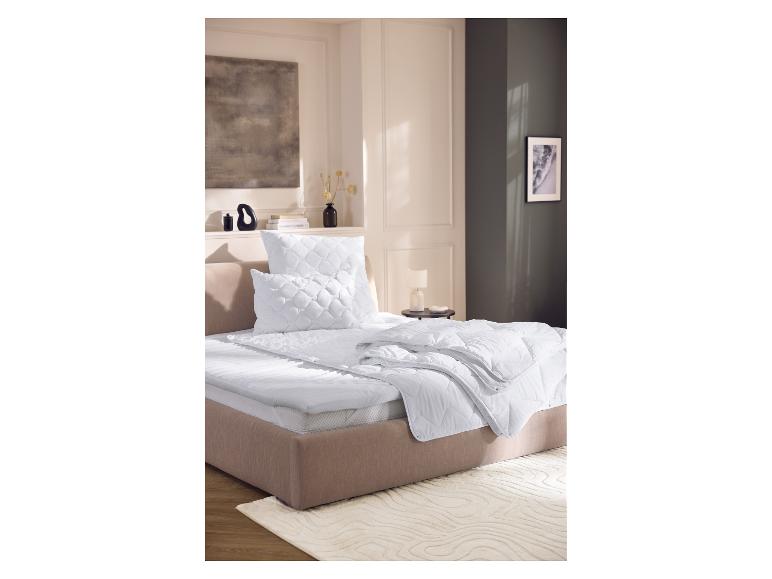 Bed met wit matras, kussens en dekbed in een moderne slaapkamer.