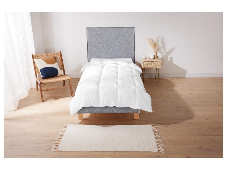 Een wit dekbed op een grijs bedframe met een vloerkleed en een stoel.