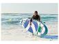 Vrouw met paddleboard en peddel, staand in het water op het strand.