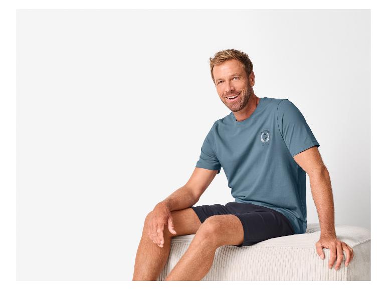 Lachende man in een blauw bedrukt T-shirt en donkerblauwe shorts.