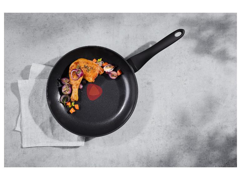 Geroosterde kippenpoot en groenten in een zwarte koekenpan op een betonnen aanrecht.