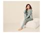 Vrouw in saliegroene pyjama zit op een witte poef, lachend en naar rechts kijkend.