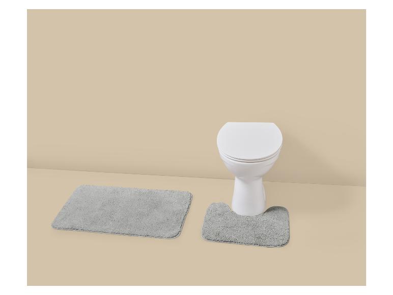 Grijze badmatten en een wit toilet in een beige badkamer.