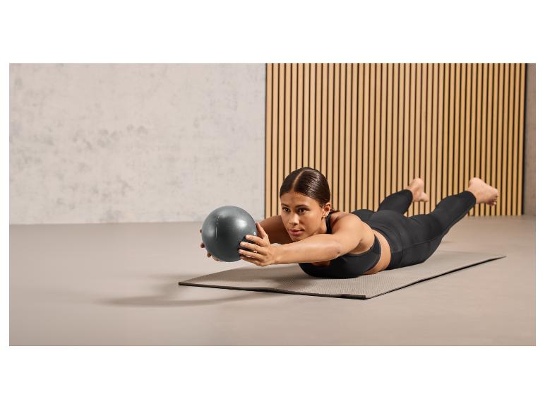 Een vrouw doet een oefening met een fitnessbal op een yogamat.