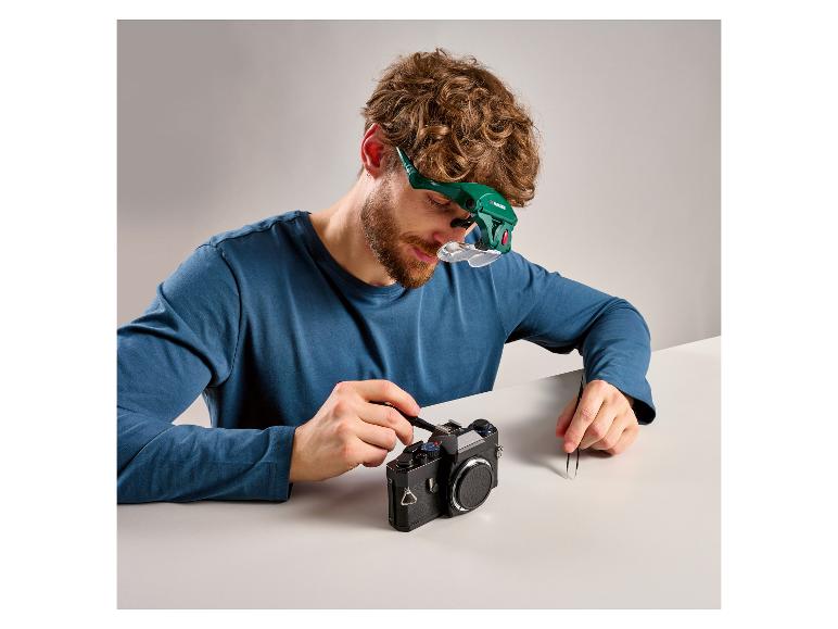 Man repareert camera met vergrootbril en gereedschap.