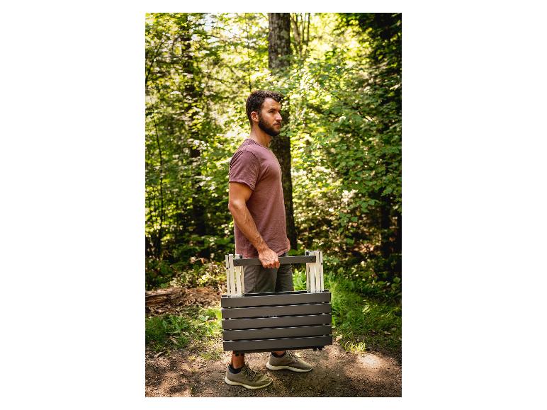 Een man draagt een opvouwbare tafel in een bos.