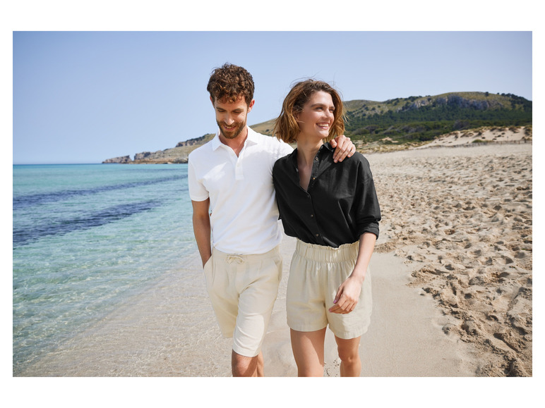 Een stel in witte en beige linnen kleding loopt op een strand.