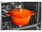Oranje geëmailleerde gietijzeren braadpan met deksel in een oven.