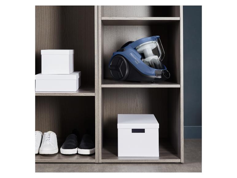 Een Rowenta stofzuiger, schoenen en opbergdozen in een houten kast.