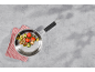 Koekenpan met gebakken tomaten, courgette en champignons op een grijze ondergrond.